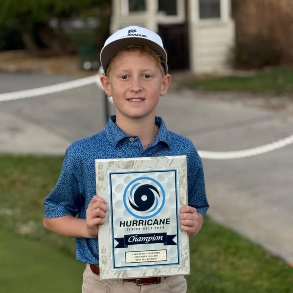 Young male junior golfer holding a Hurricane Junior Golf Tour Champion award plaque and smiling after winning the Boys 10-11 division.